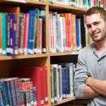 Smiling male student leaning on a shelf in a library
