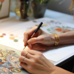 ידים של אישה מציירת עם עט ציור צבעוני על שולחן כחלק מטיפול במאנויות